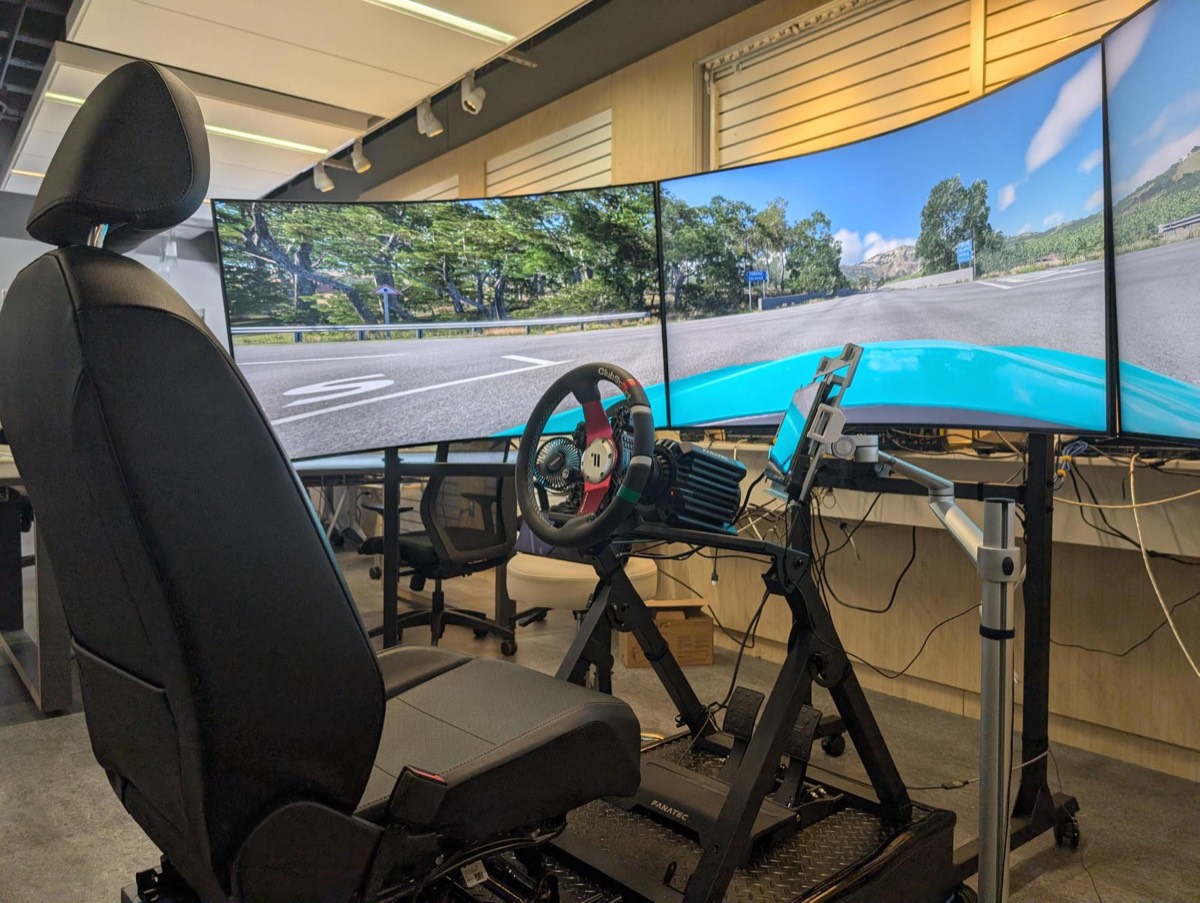 The driving simulator: a car seat, a steering wheel and pedals, before three curved screens.