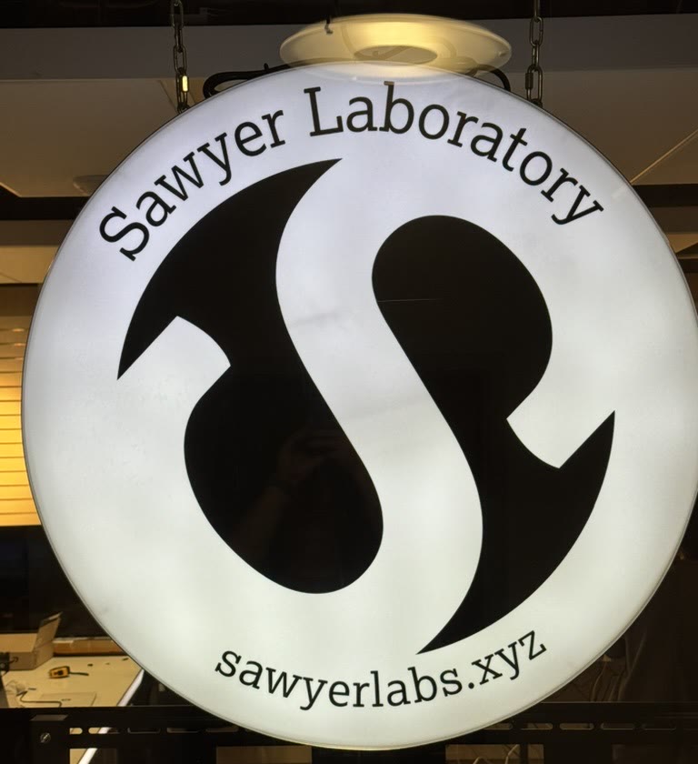 The lab’s round lit sign, Sawyer Laboratory, sawyerlabs.xyz.
