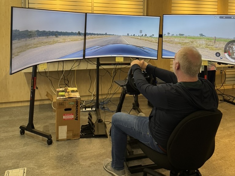 A guest at the wheel of the lab’s driving simulator, its three curved screens showing a country road.